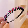 A hand holds a black elastic hair hoop decorated with colorful sparkling rhinestones.