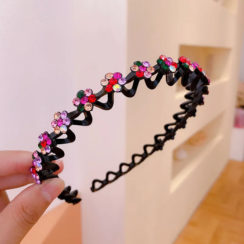 A hand holds a black elastic hair hoop decorated with colorful sparkling rhinestones.