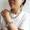A close-up of a woman wearing a silver boho punk twisted link necklace and bracelet against a white shirt.