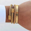 A gold stainless steel bracelet featuring Roman numerals and a braided cord, worn on a wrist.