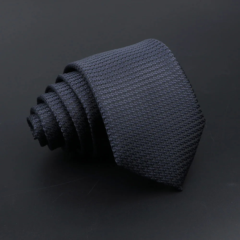 A dark gray knitted tie with plaid dots is shown rolled and folded on a black surface.