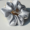 A cluster of silky gray hair scrunchies gathered in a rosette shape on a light background.