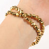 A stack of gold-plated hematite round cube beads for DIY jewelry is shown on a wrist.