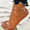 Gold and silver heart chain anklets worn on a foot against a sandy background.