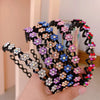 A hand holds a black elastic hair hoop decorated with colorful sparkling rhinestones and small flowers.