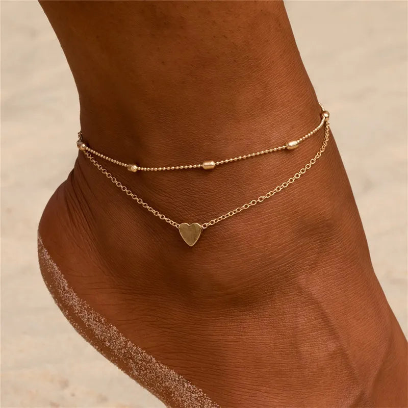 Gold and silver heart chain anklets worn on a person's foot.