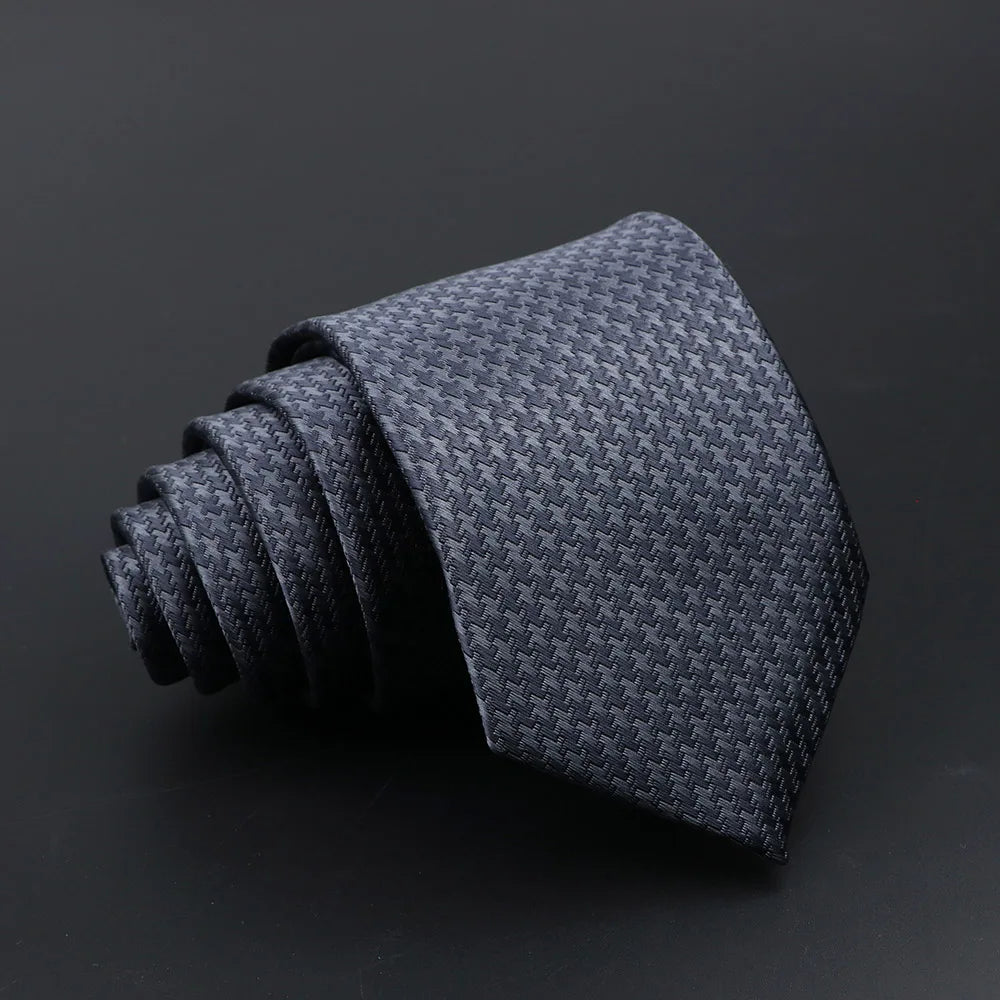 A dark gray woven tie folded and displayed against a black background.