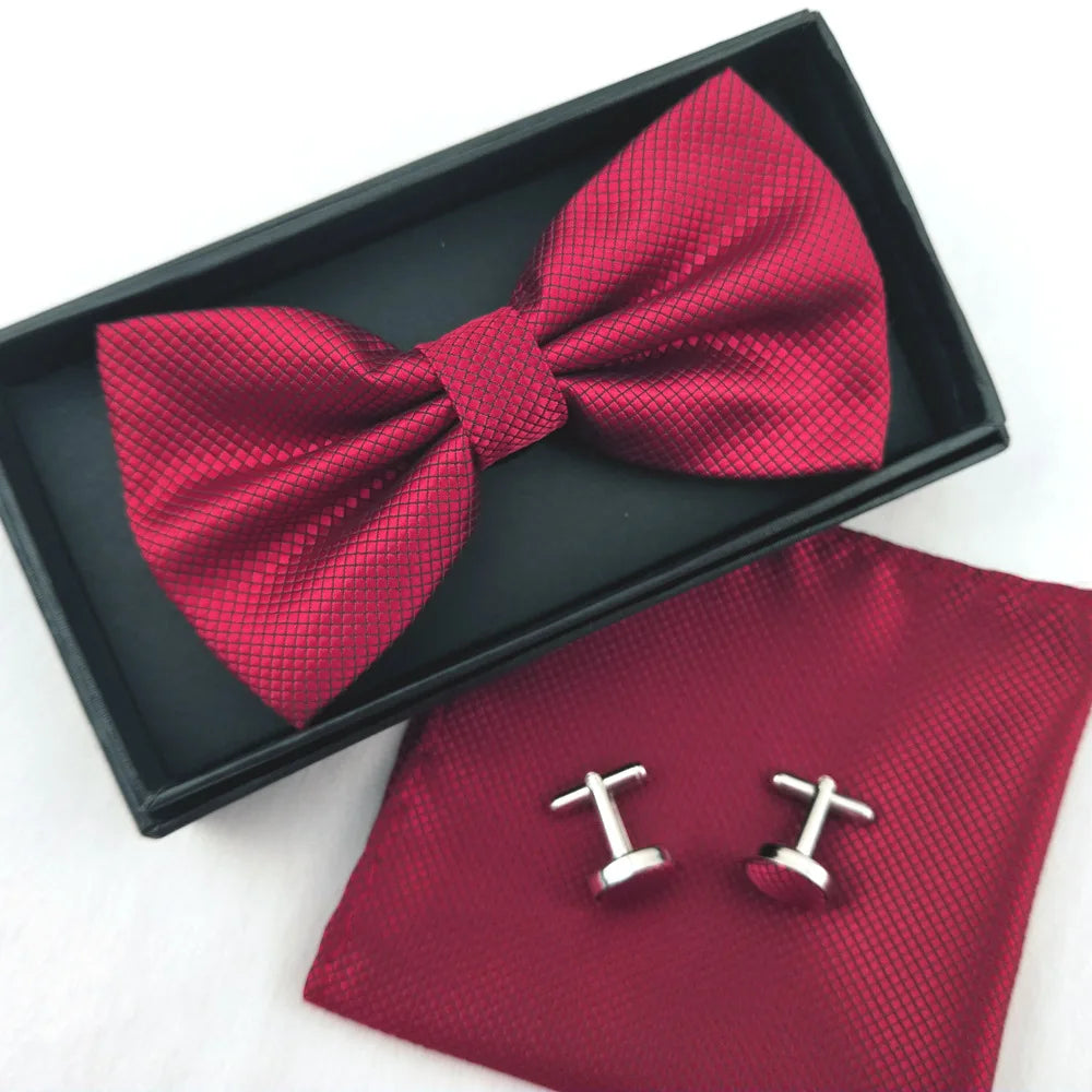 A dark box holds a red patterned bow tie and silver cufflinks on a maroon cloth background.