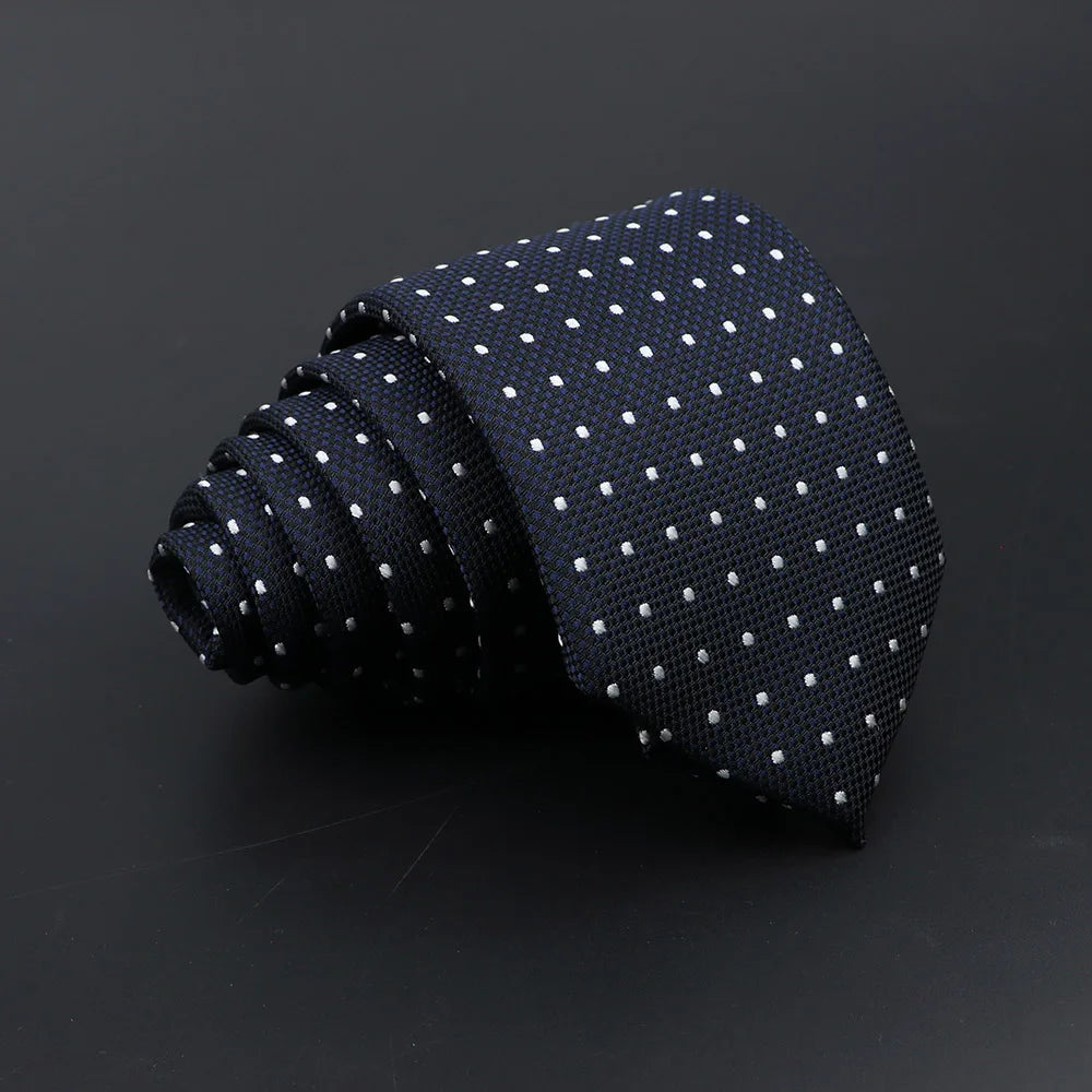 A dark blue classic men's tie with small white polka dots, rolled and displayed on a dark surface.