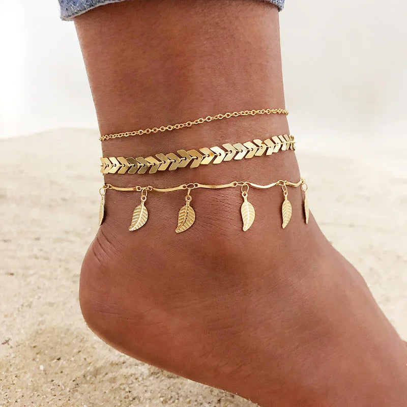Gold stainless steel leaf anklets worn on a person's foot.
