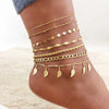 A collection of layered gold stainless steel anklets worn on a person's ankle.