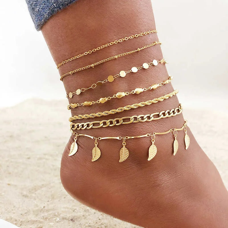 A collection of layered gold stainless steel anklets worn on a person's ankle.