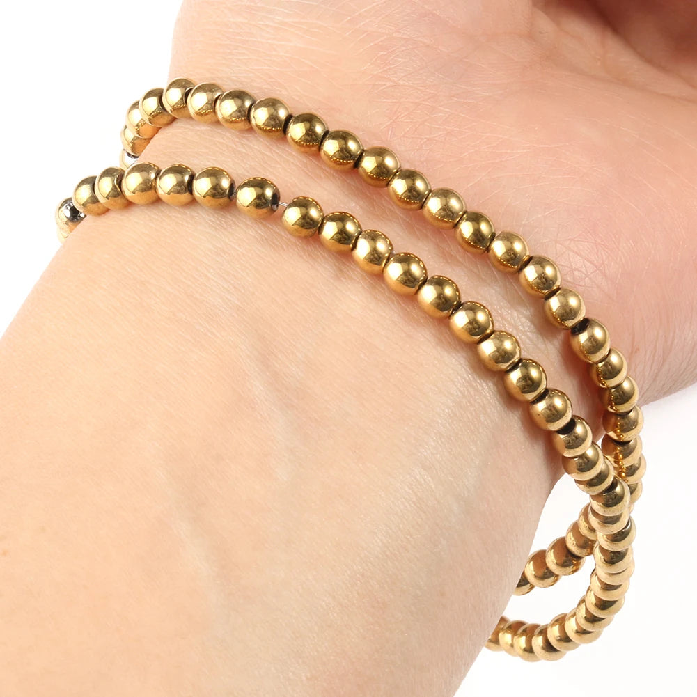 A hand is holding several strands of gold-plated hematite round cube beads for DIY jewelry.