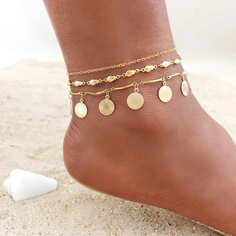 Gold stainless steel anklets for women layered on a foot against a light background.