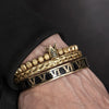Primer plano de una mano con pulseras apiladas de esmalte dorado y negro con números romanos.