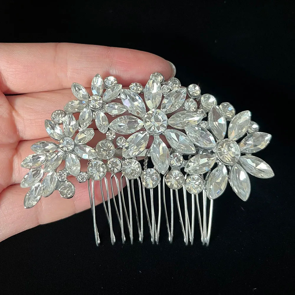 A silver rhinestone bridal hair comb tiara with floral clusters and dangling strands is held in a hand.