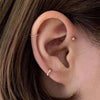 Close-up of a woman's ear showing minimalist gold hoop earrings against dark hair.