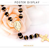 Collar de cruz de Virgen María de acero inoxidable dorado con cuentas negras y cadena extensible, exhibido en una rosa rosa.