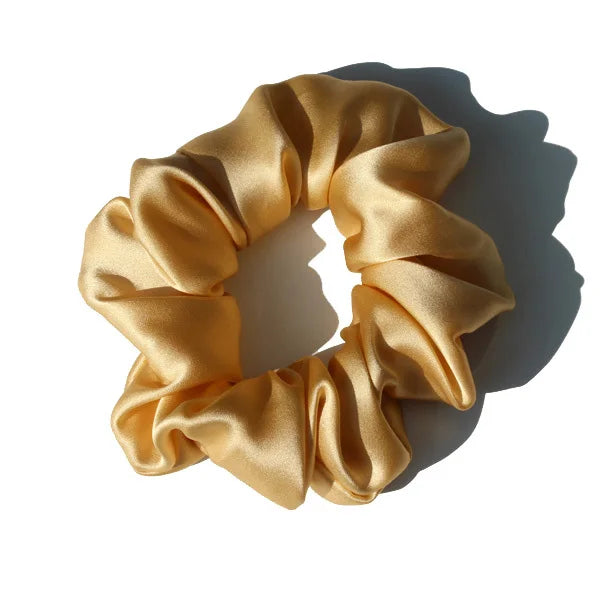 A close-up of a golden yellow silk hair scrunchie tied in a bow shape.