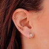 Close-up of a woman's ear showing minimalist gold hoop earrings and a small heart stud.