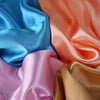 Primer plano de pañuelos de seda satinada drapeados en tonos azules, melocotón, rosa y dorado.