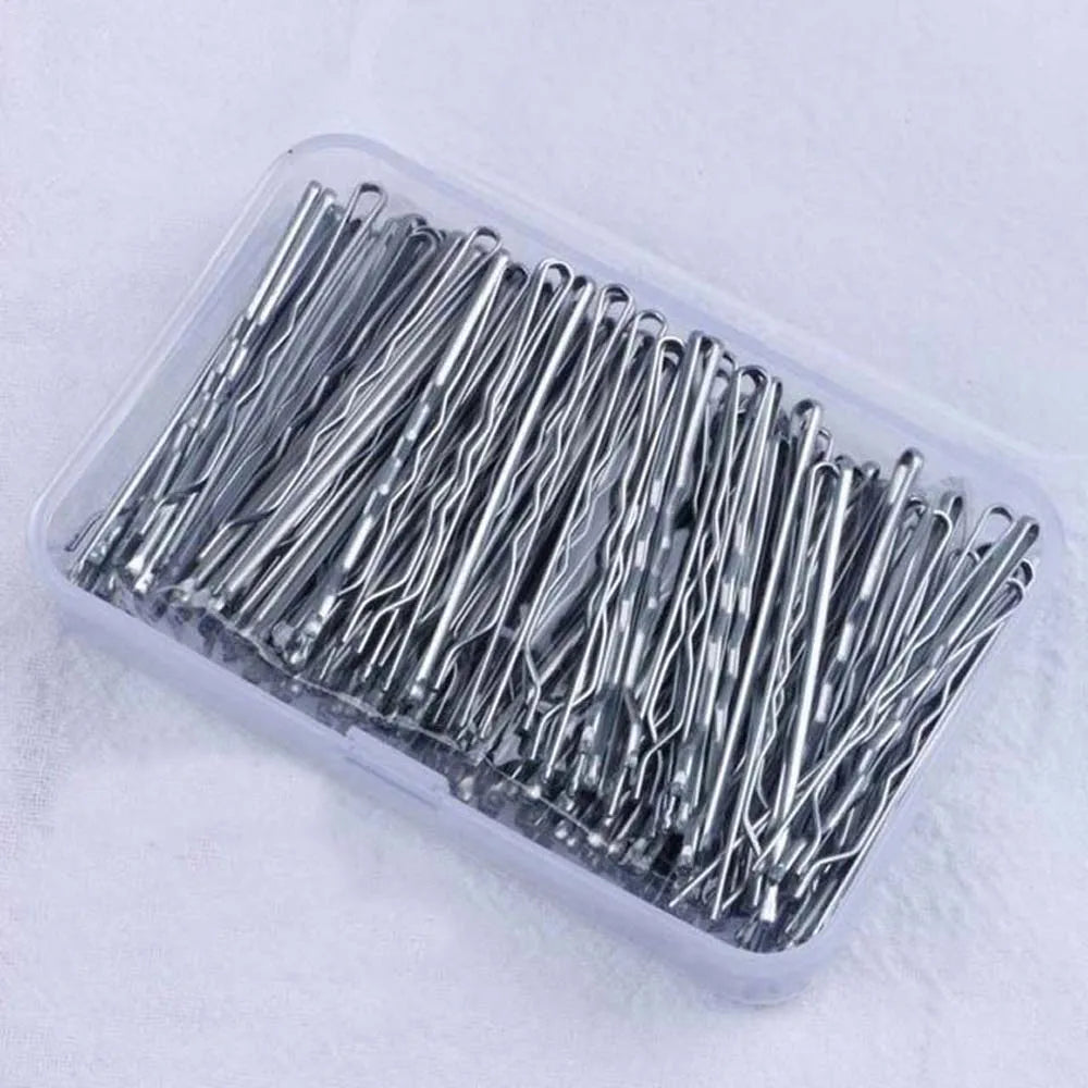 A clear plastic container filled with numerous thin, silver metal hair clips for styling.