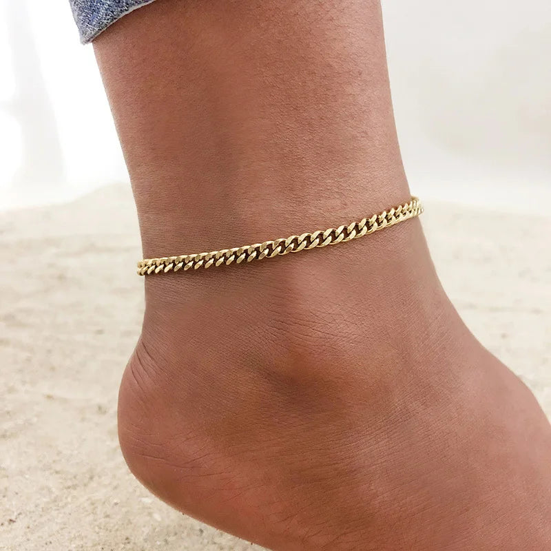 A close-up of a gold stainless steel chain anklet worn around a person's ankle.