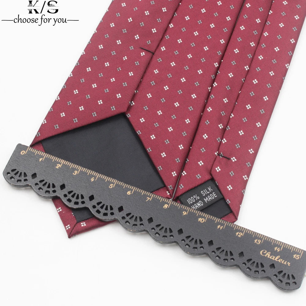 A close-up of a maroon patterned necktie with a black square, shown next to a measuring ruler.