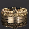 Pulseras de esmalte dorado y negro con números romanos apilados sobre una superficie reflectante.