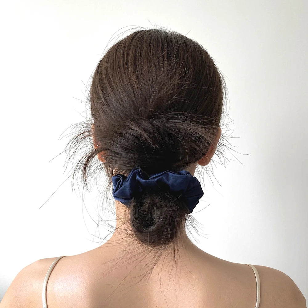 A dark brown hair tied in a messy bun with a navy blue silk scrunchie on the back of the head.