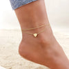 Gold stainless steel anklets with heart charms worn on a woman's ankle.