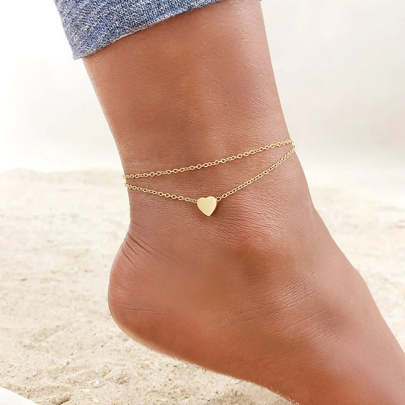 Gold stainless steel anklets with heart charms worn on a woman's ankle.