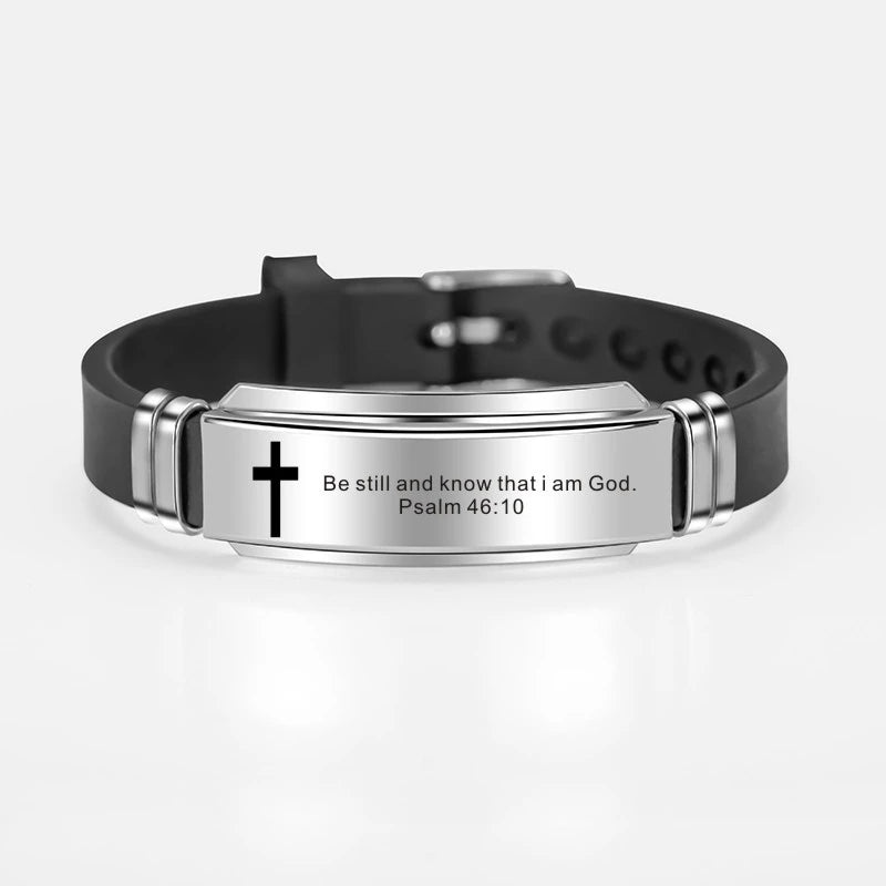A black leather bracelet with a silver plate engraved with the text Be still and know that I am God Psalm 46:10