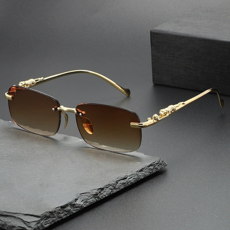 Rimless square sunglasses with gold-toned metal frames resting on a dark gray slate surface.