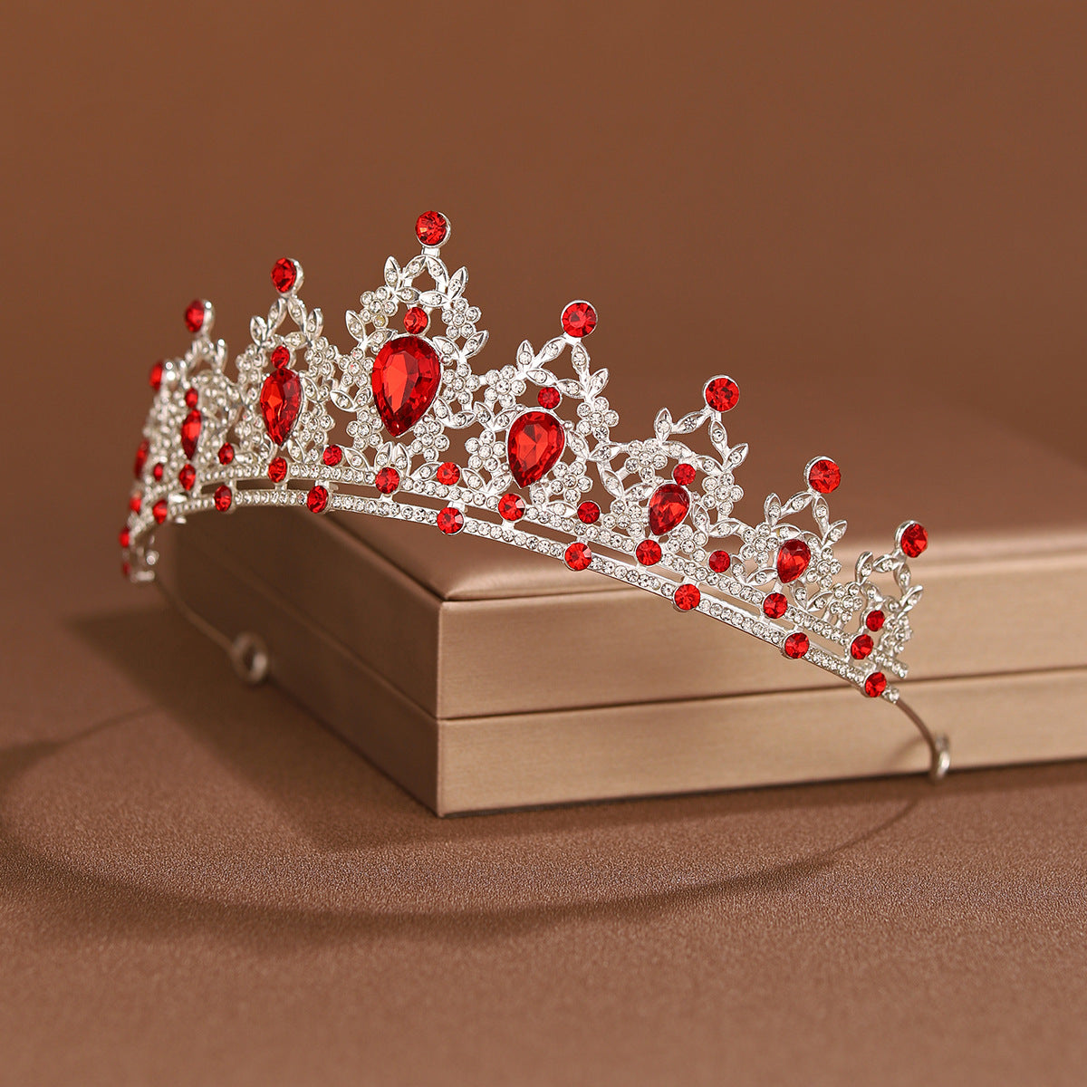 An elegant crystal baroque bridal tiara headpiece with red gemstones resting on a light brown box.