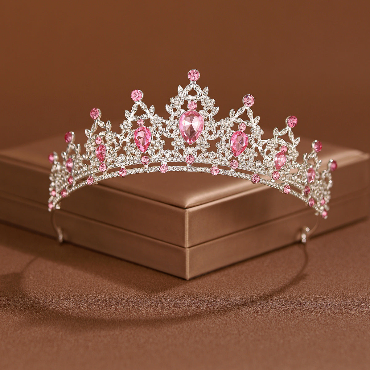 A sparkling crystal baroque bridal tiara headpiece with pink and clear stones resting on a brown box.