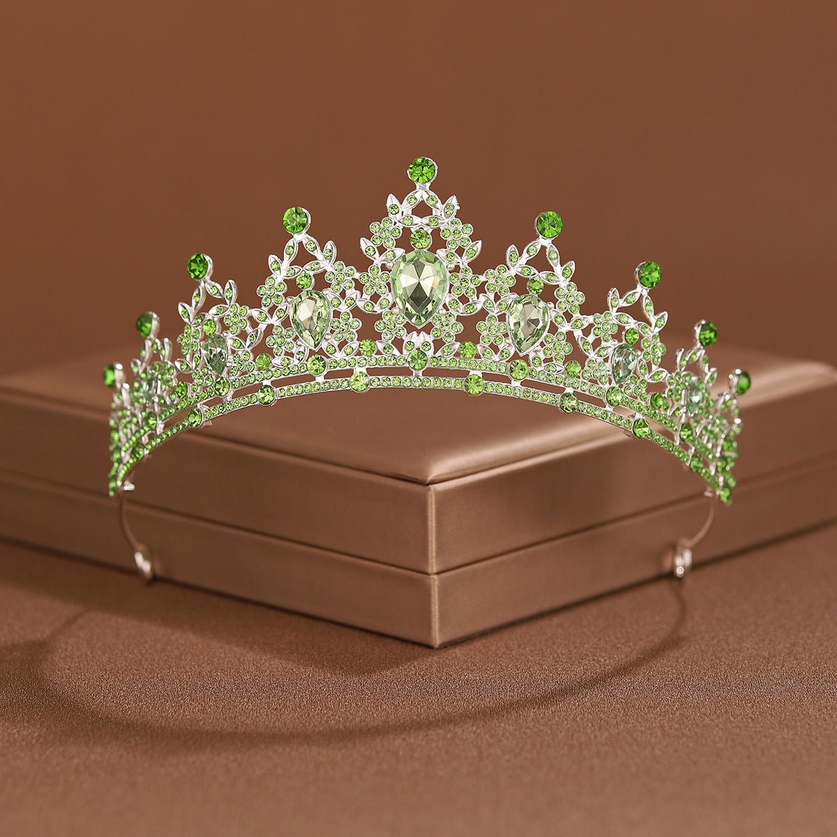 A sparkling crystal baroque bridal tiara headpiece with green gemstones resting on a brown box.