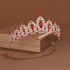 A sparkling crystal baroque bridal tiara headpiece with red gemstones displayed on a box.