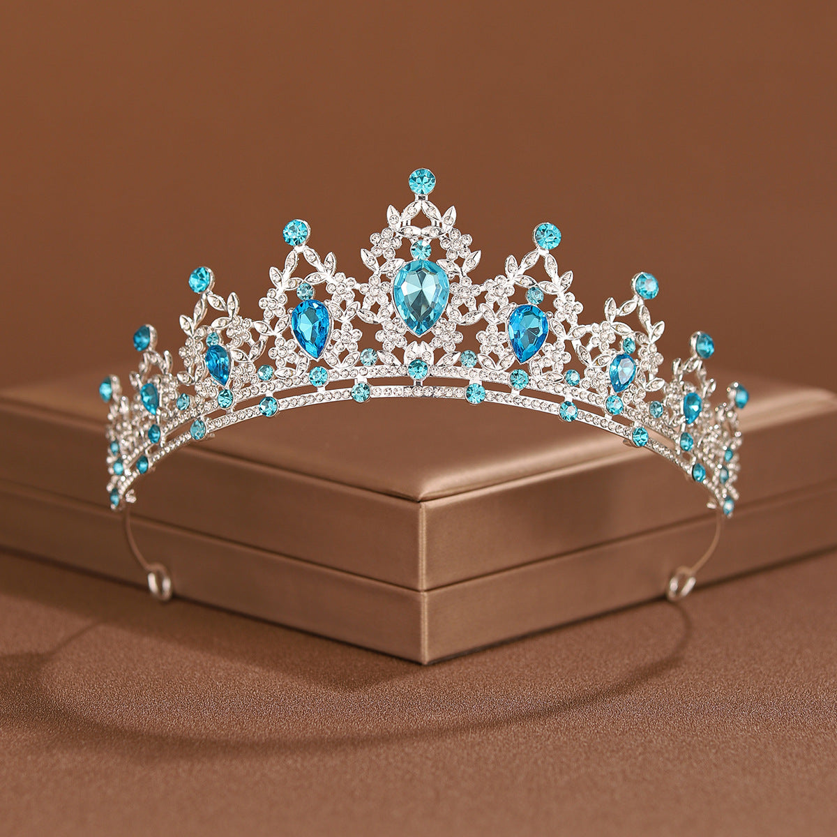An elegant crystal baroque bridal tiara headpiece featuring blue gemstones and clear crystals displayed on a box.