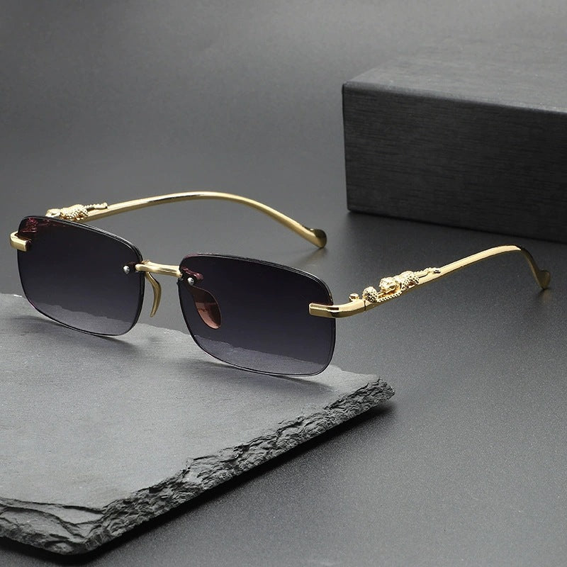 Gold-framed rimless square sunglasses resting on a dark slate surface.