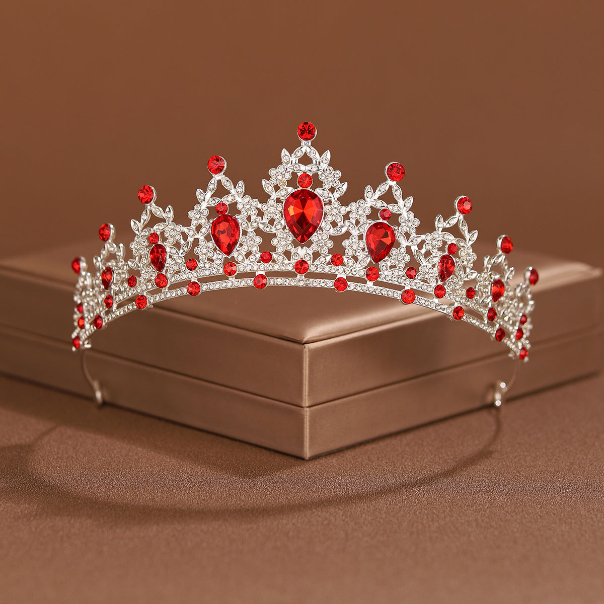 An elegant crystal baroque bridal tiara headpiece with red gemstones resting on a brown box.
