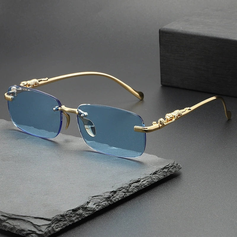 Gold-rimmed rimless square sunglasses with blue mirrored lenses resting on a dark gray surface.