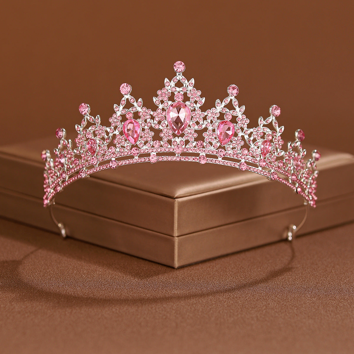 A pink crystal baroque bridal tiara headpiece displayed on a brown box.