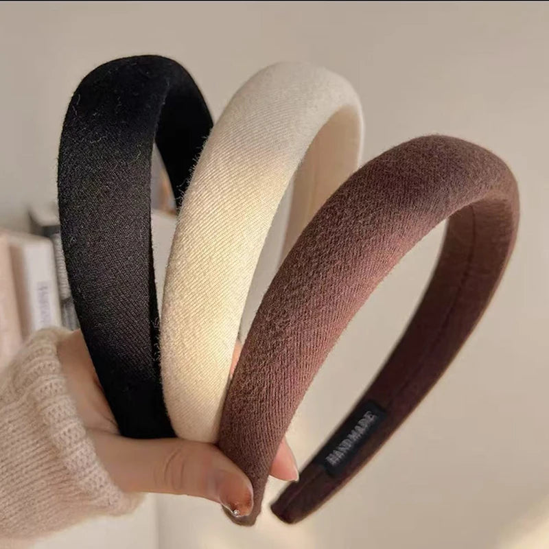 Une main tient un bandeau pour cheveux épaissi de couleur café dans les tons noir, crème et brun.