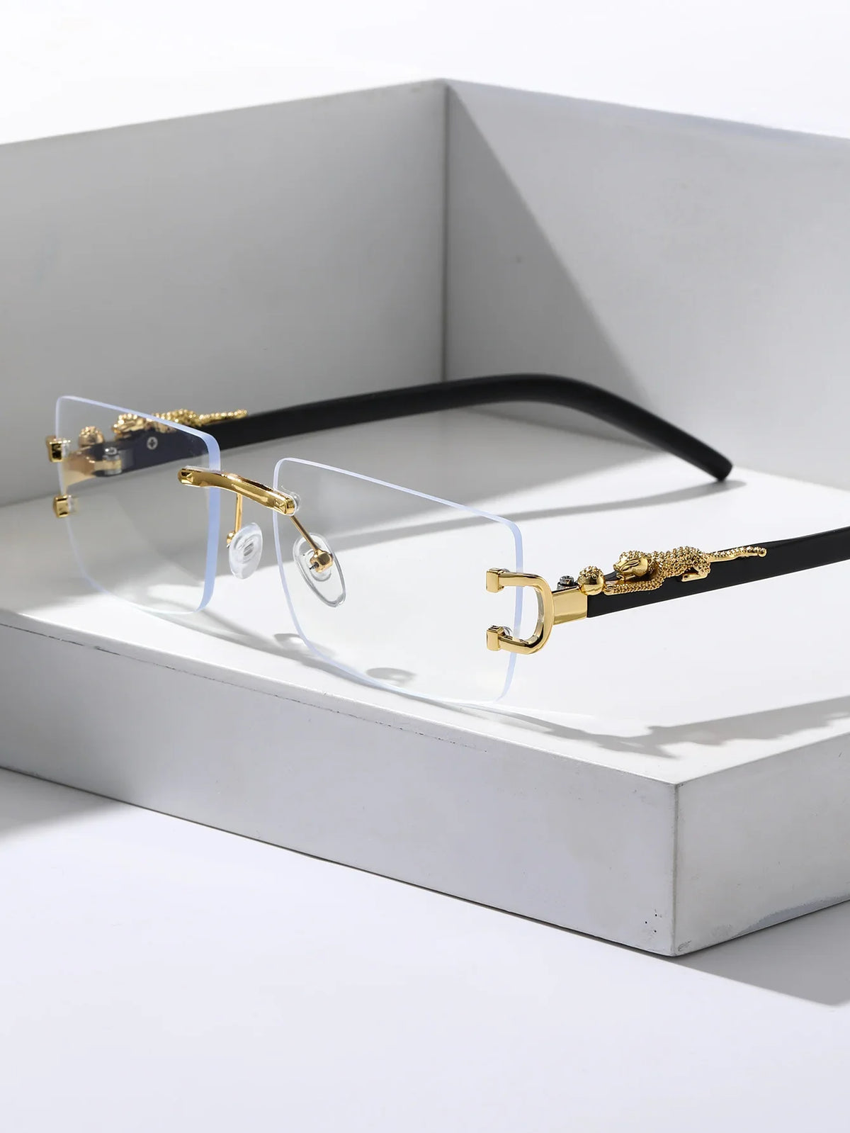 A pair of trendy frameless rectangular sunglasses with gold-toned metal accents and black frames displayed in a white box.
