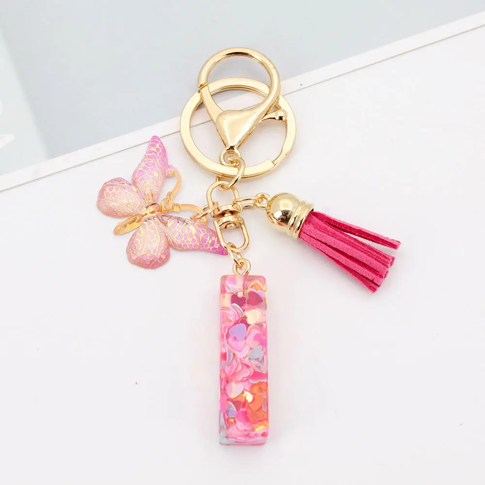 Gold acrylic letter keychain with a pink butterfly charm and a magenta tassel