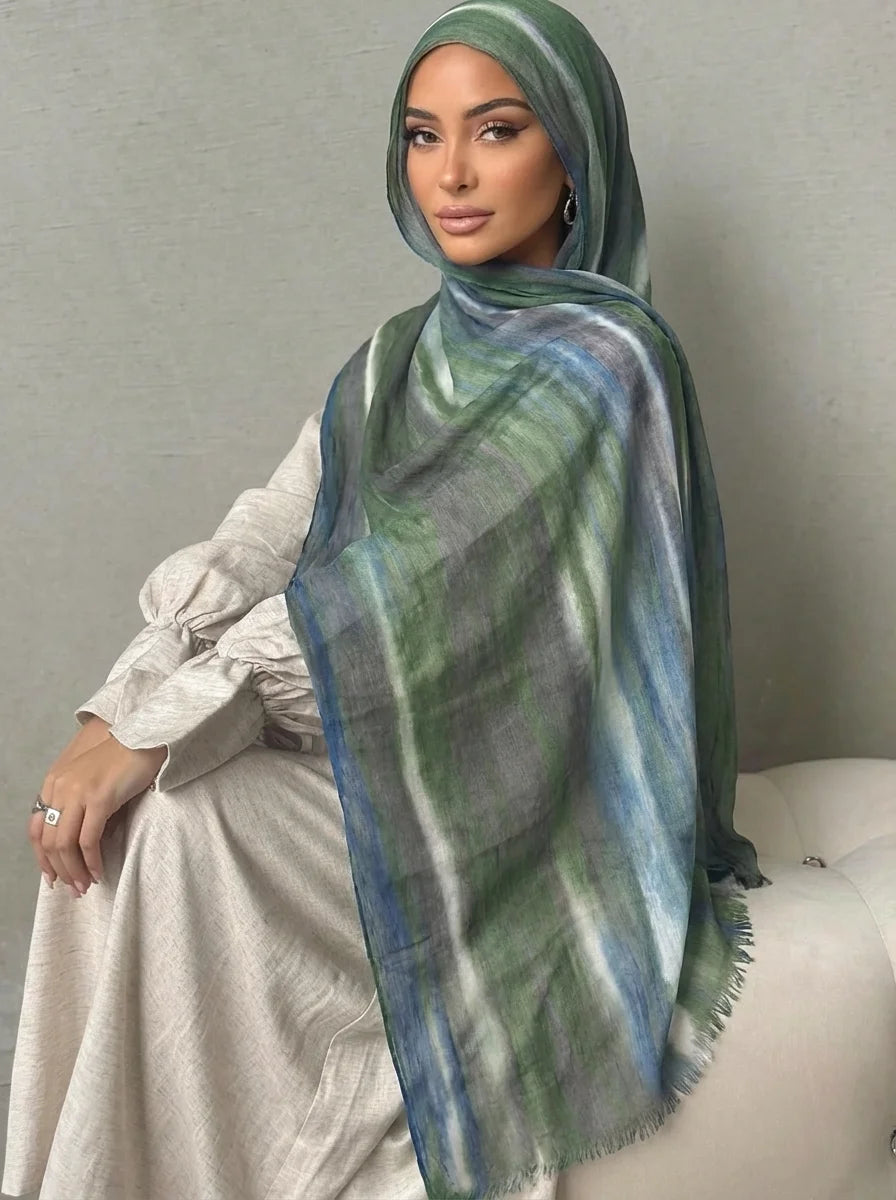 Una mujer vistiendo un elegante pañuelo de hijab a rayas verdes y azules con una blusa beige clara.