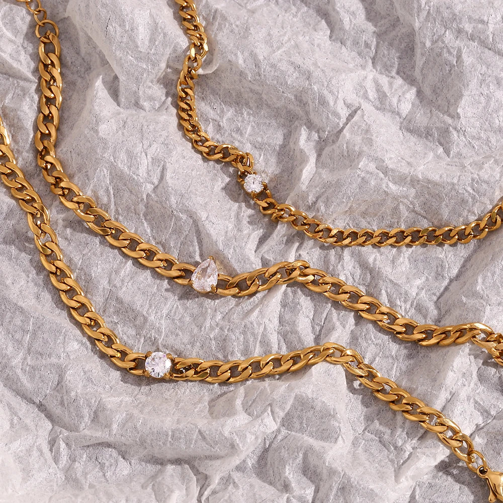 Gold chain bracelet with round water drop zircon charms laid on wrinkled white paper.