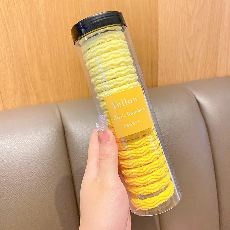 Contenedor de plástico transparente lleno de una liga para el pelo con rayas onduladas amarillas, etiquetada como Yellow Girl