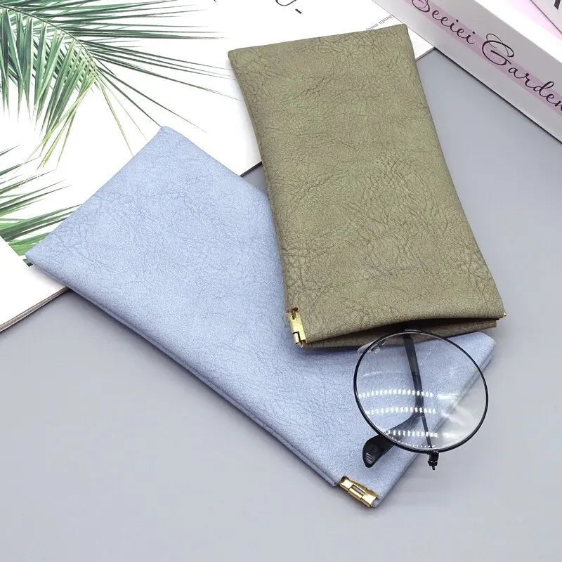 A stack of premium PU leather eyewear storage bags in light blue and olive green colors with a pair of round glasses.